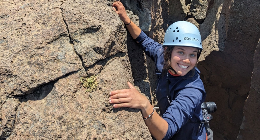 A person wearing safety gear is secured by ropes as they climb a rock wall. 